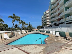 A swimming pool with lounge chairs, palm trees, and a multi-story building with balconies. - Ocean Sunset Lover (Isabela)