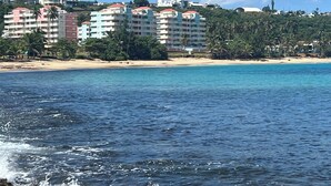 Ett hotell vid kusten med flera våningar, som ligger direkt vid stranden och har palmer.