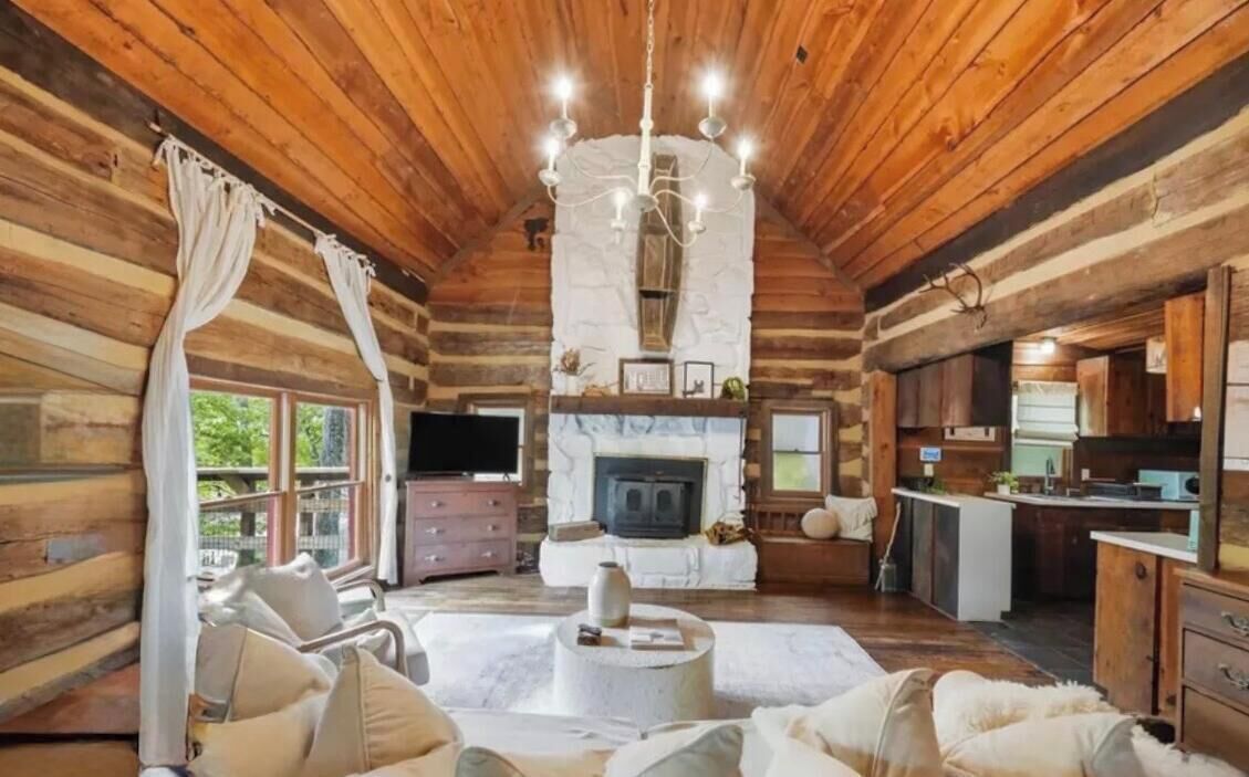 L’intérieur d’une cabane en rondins, avec une cheminée, des murs en bois, un lustre et un coin salon confortable.