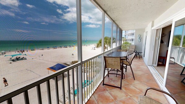 Ein Balkon mit Blick auf einen Strand, einem Tisch, Stühlen und einem Geländer.