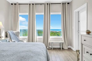Ein Schlafzimmer mit einem großen Bett, einer Bank, Meerblick und einer weißen Kommode.