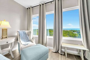 Ein Zimmer mit Blick auf eine Landschaft, ein weißer Stuhl, eine Bank, eine Lampe und ein kleiner Tisch.