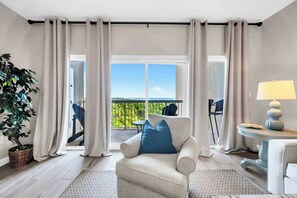 Ein modernes Wohnzimmer mit einer Couch, einer Lampe und Blick auf einen Balkon mit Gartenmöbeln.