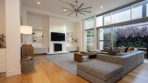 A modern living room with a fireplace, a large grey sofa, a coffee table, and a TV mounted on the wall. - Margaret House | Elegant City-Fringe Escape (North Adelaide)