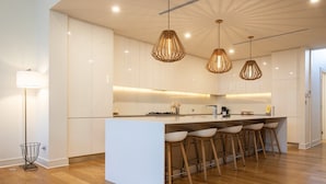 A modern kitchen with a central island, bar stools, pendant lighting, and wooden flooring. - Margaret House | Elegant City-Fringe Escape (North Adelaide)