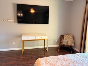 Ein Hotelzimmer mit Bett, Schreibtisch, Stuhl, Wand-Fernseher und einem Fenster mit Vorhängen.