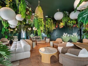 Ein Zimmer mit einer Couch, Sesseln, einem Couchtisch, hängenden Pflanzen und einer Pendelleuchte.