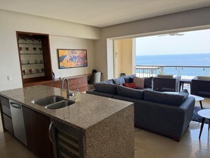 A modern kitchen with granite countertops, a built-in sink, and a dining area with a view of the ocean. - Amazing ocean view 1 Bedroom condo in Conchas Chinas. (Puerto Vallarta)