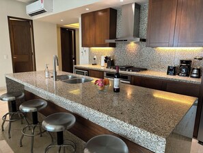 A modern kitchen with granite countertops, stainless steel appliances, and wooden cabinets. - Amazing ocean view 1 Bedroom condo in Conchas Chinas. (Puerto Vallarta)
