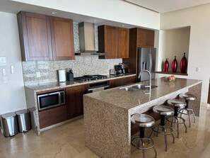 A modern kitchen with granite countertops, stainless steel appliances, and wooden cabinets. - Amazing ocean view 1 Bedroom condo in Conchas Chinas. (Puerto Vallarta)