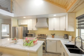 A modern kitchen with white cabinets, a stainless steel stove, a microwave, and a sink.
