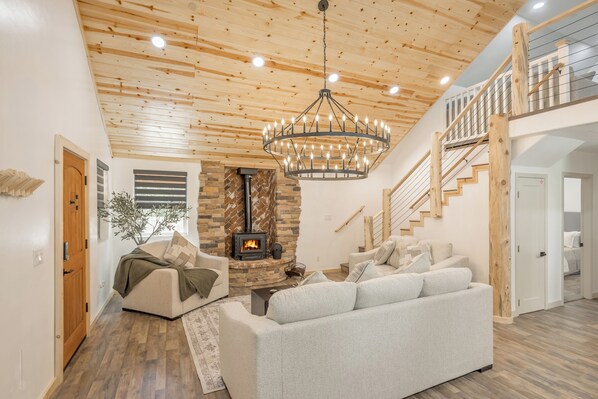 A living room with a stone fireplace, a chandelier, and a staircase.