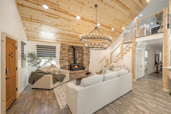 A modern living room with a fireplace, wooden ceiling, and a staircase leading to an upper level.
