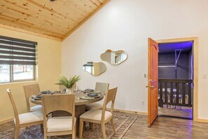 Un coin repas avec un plafond en bois, une table ronde, des chaises, une plante en pot et une porte donnant sur un balcon.
