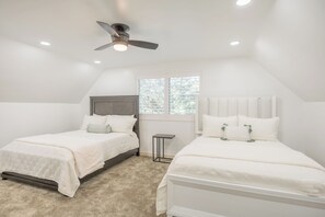 Une chambre avec deux lits, un ventilateur de plafond, une fenêtre et un radiateur.