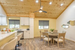 A modern kitchen with white cabinets, a wooden ceiling, and a dining area with a table and chairs.