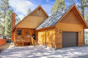 Une cabane en rondins à deux étages, dotée d’un porche à l’avant, d’un garage et d’un escalier menant à l’étage supérieur.