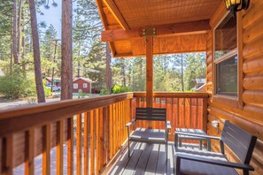 A wooden deck with two chairs and a table, surrounded by a wooden railing, overlooking a forested area.
