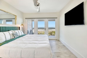 Ein Schlafzimmer mit Bett, Fernseher, Balkon mit Meerblick und einem Sessel.