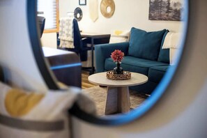 Una sala de estar con un sofá azul, una mesa redonda de centro con una flor, y un comedor al fondo.