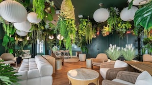 Een kamer met een bank, stoelen, een salontafel, hangende planten en een hanglamp.