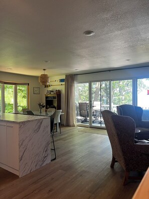 A spacious living area with a marble kitchen island, a dining table with chairs, a large window with a view of greenery, and a patterned armchair. - 4-bedroom Leech Lake Retreat on Quiet Agency Bay (Walker)