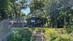A wooden house with a balcony, surrounded by trees and a grassy area.