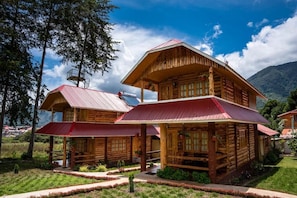 Una cabaña de madera con techo rojo, rodeada de un jardín cuidado y un paisaje montañoso.