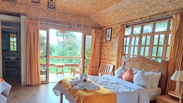 Un dormitorio de cabaña de madera con cama, un banco, una mesa y vistas al exterior.