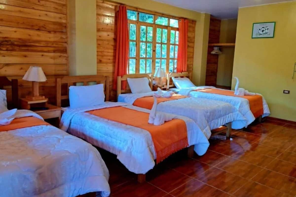 Una habitación con cuatro camas, paredes de madera, una ventana con cortinas y suelo de baldosas.
