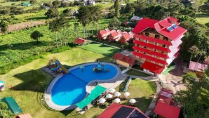 Un hotel con piscina, mobiliario exterior y un edificio de tejado rojo.