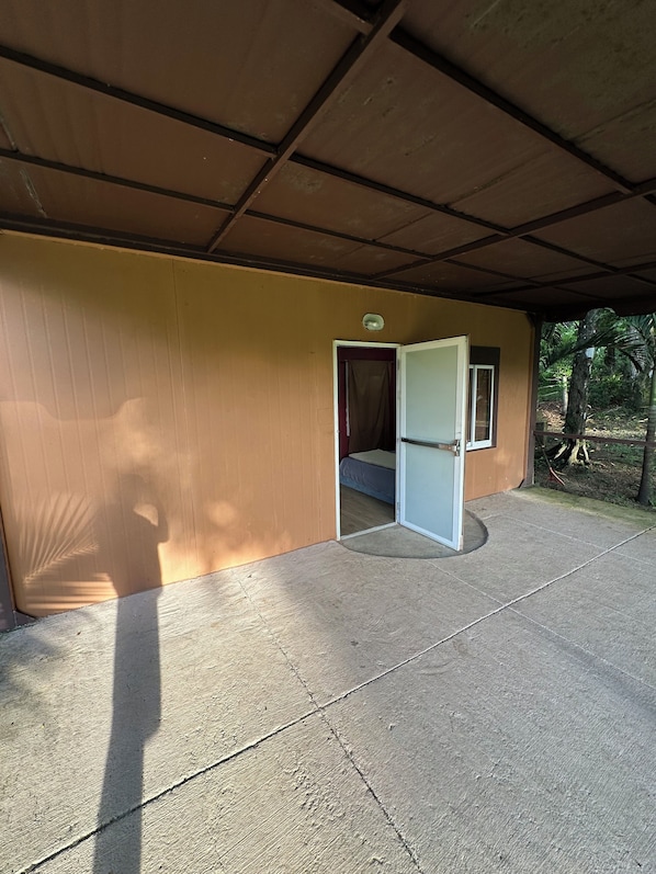 A covered outdoor area with a concrete floor, a door leading to a room, and a small window.