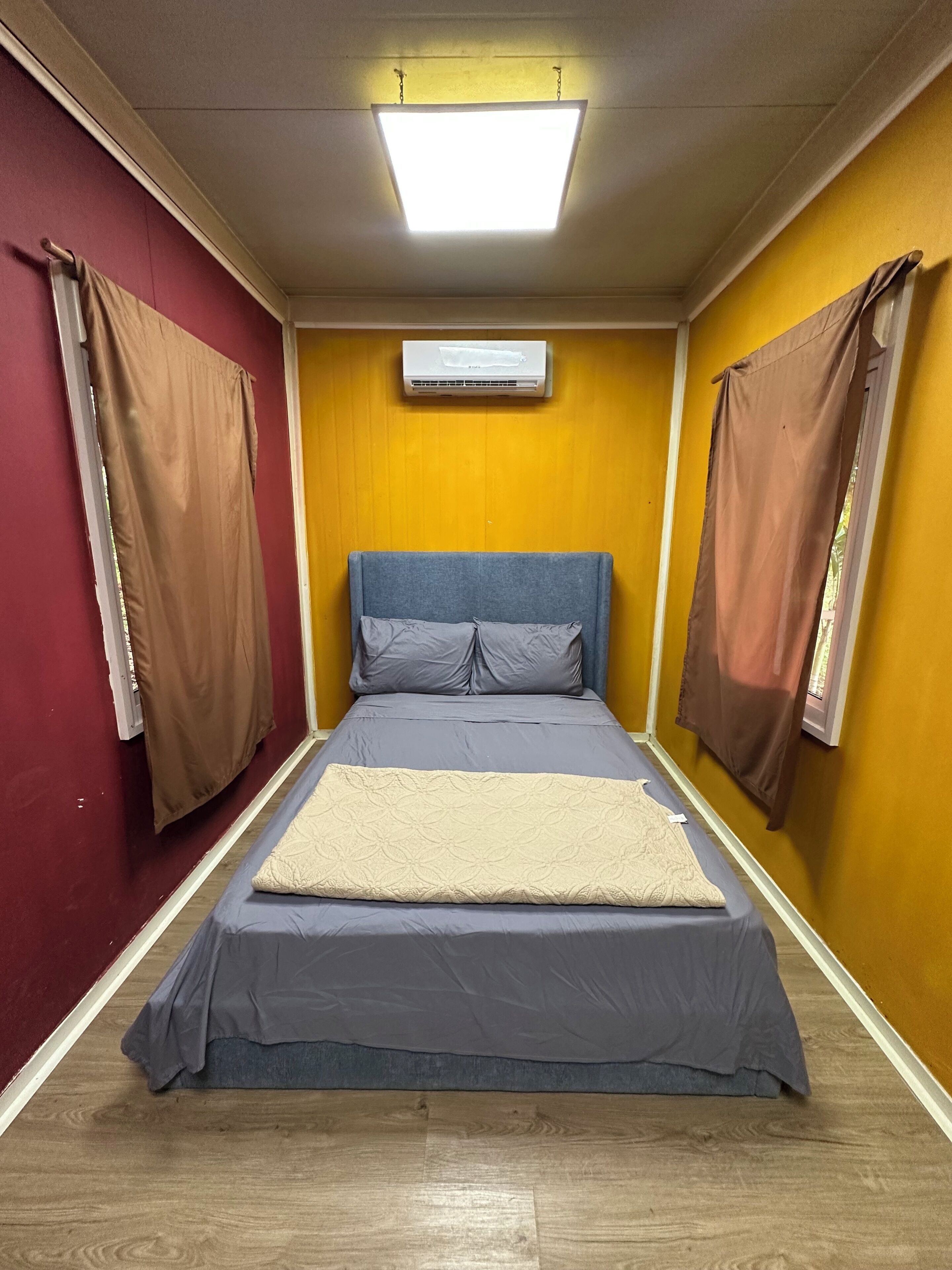A room with a bed, curtains, an air conditioning unit, and a wooden floor.