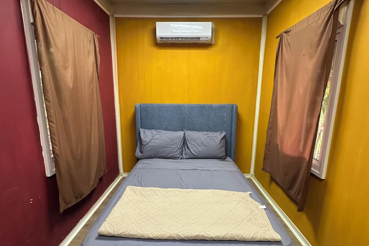 Une chambre avec un lit, des rideaux, un appareil de climatisation et un plancher en bois.