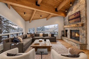 Ein gemütliches Wohnzimmer mit Kamin aus Stein, großen Fenstern und Holzboden.