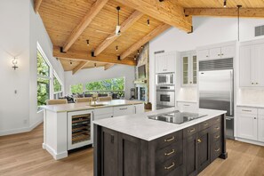 A modern kitchen with a large island, white cabinetry, stainless steel appliances, and a wooden ceiling.