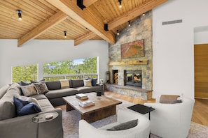 A spacious living area with a stone fireplace, a large window, and a wooden ceiling.