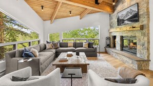 Una sala moderna con chimenea de piedra, ventanas amplias y techo de madera.