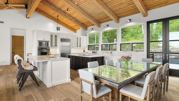 Una cocina moderna con armarios blancos, una isla central y una zona de comedor con una mesa de vidrio y sillas.