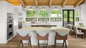 Una cocina moderna con armarios blancos, electrodomésticos de acero inoxidable, techo de madera y ventanas amplias.