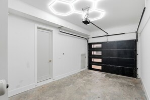 A garage with white walls, a black garage door, and a ceiling light fixture. - Fully Custom New Construction In the Heart of Midtown (Atlanta)