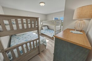 Ein Zimmer mit Etagenbetten, einem Schreibtisch, einer Lampe und einem Fenster.