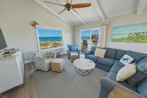 Ein Wohnzimmer mit Blick auf den Strand, einem Deckenventilator und einem Sofa mit einem Kissen in Form eines Krebsses.