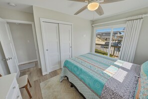 Ein Schlafzimmer mit einem Bett, einem Deckenventilator, einem Fenster mit Vorhängen und Blick auf einen Balkon.