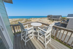 A wooden deck with a round table and white chairs, overlooking a beach and dunes. - South Nags Head 426: Semi-Oceanfront, Ocean Views, Hot Tub (Nags Head)