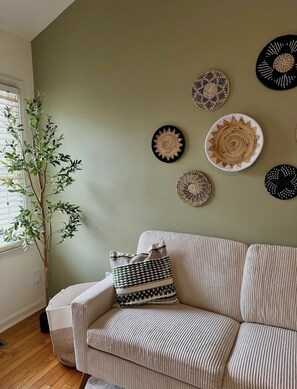 Une pièce avec un canapé beige, une petite plante et plusieurs décorations murales tissées.