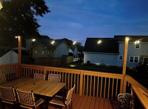 En træterrasse med et bord og stole, omgivet af et træhegn, med udsigt over et boligområde med huse.