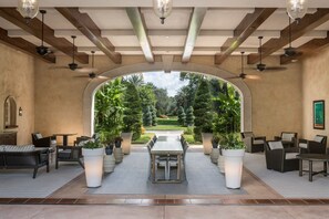 Ein überdachter Innenhof mit Esstisch, Stühlen, Topfpflanzen und Blick auf einen Garten.