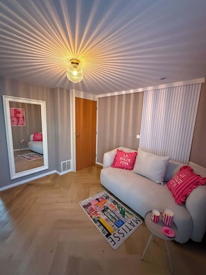 Ein modernes Wohnzimmer mit einer Couch, einem Spiegel, einer Holztür und einer Deckenleuchte.