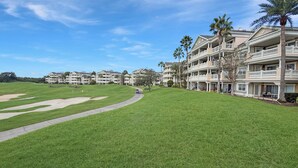 Un campo da golf con un vialetto, un edificio con molti balconi e palme.